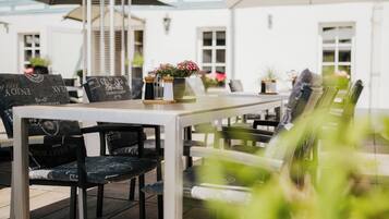 An outdoor dining area with a table and chairs, a potted plant, and a building in the background.