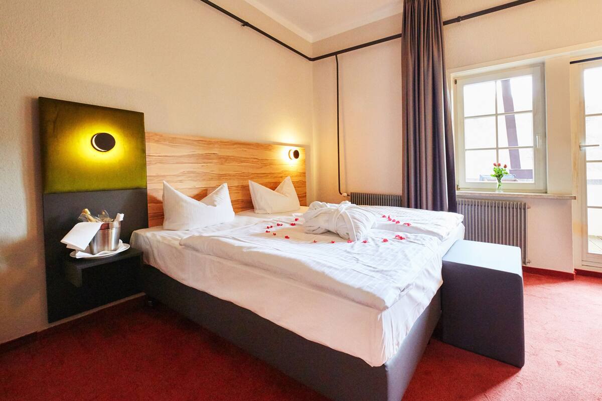 A hotel room with a bed, bedside tables, a wall art piece, a window with curtains, and a radiator.