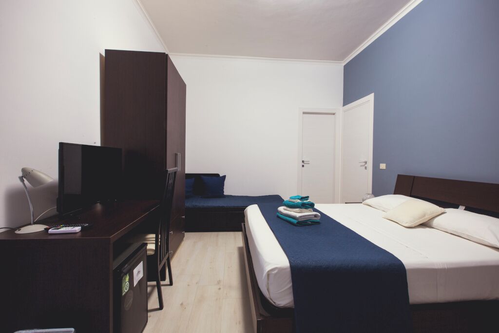 A hotel room with a bed, a desk with a TV, a wardrobe, and a door.