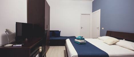 A hotel room with a bed, a desk with a TV, a wardrobe, and a door.