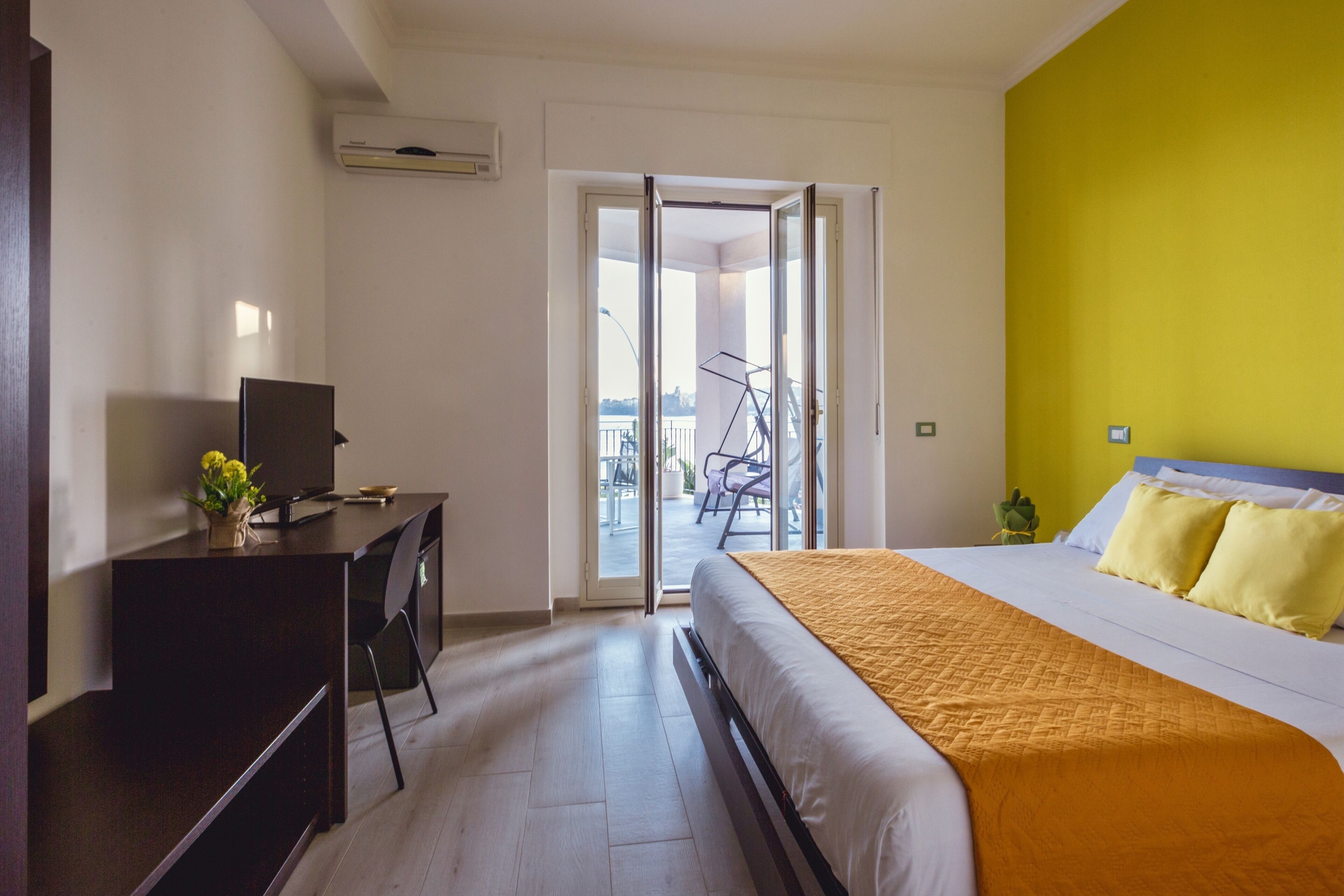 A hotel room with a bed, a desk, and a chair. There is a sliding door leading to an outdoor area with a bicycle and a table.