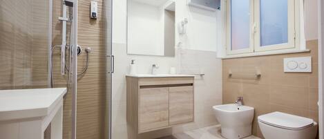 A modern bathroom with a glass shower enclosure, a wooden vanity, a bidet, and a toilet.