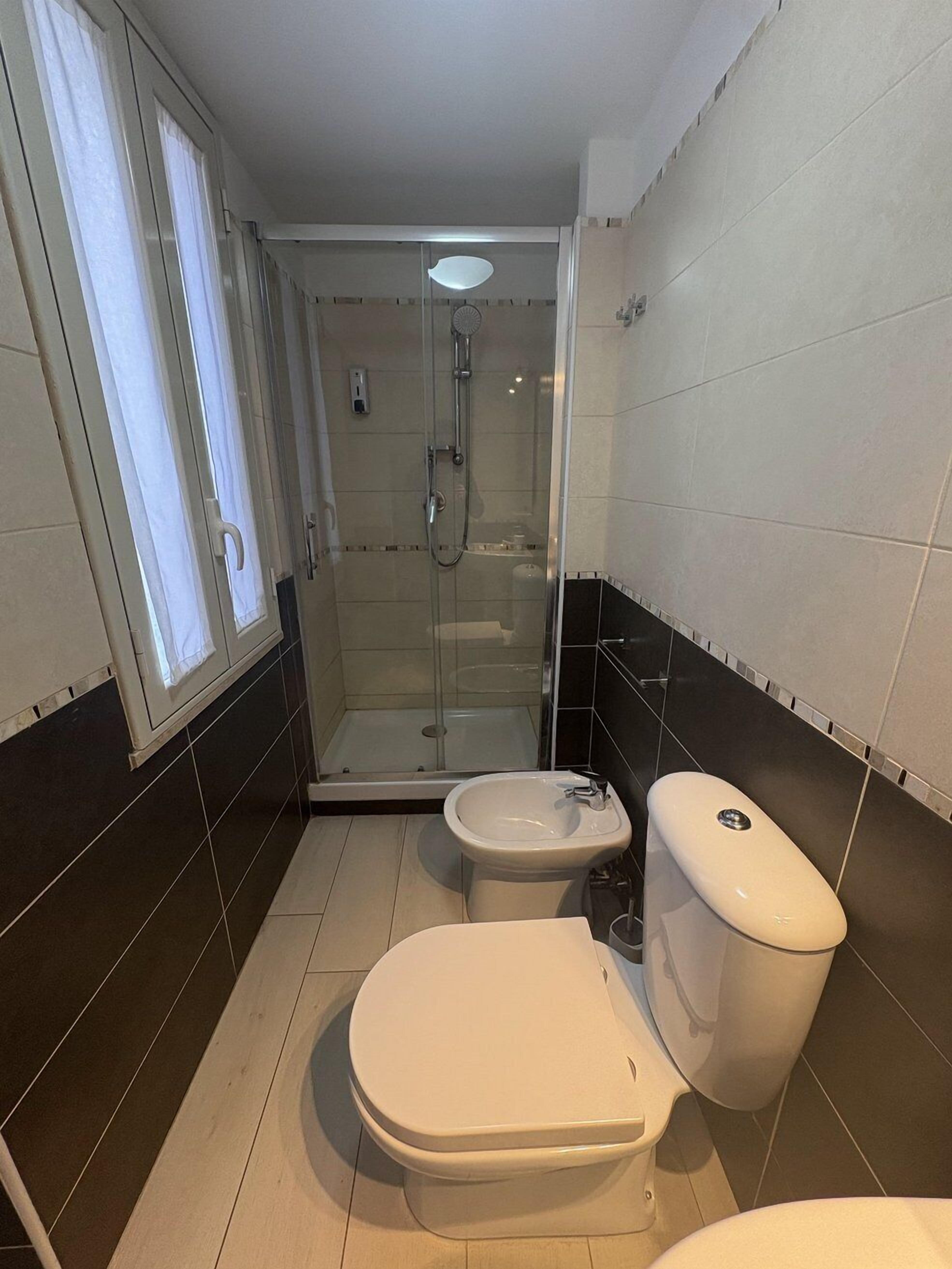 A compact bathroom with a glass-enclosed shower, a toilet, and a bidet.