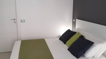 Ein ordentlich bezogenes Bett mit einer weißen Matratze, einer grünen Tagesdecke und zwei Kissen, eines schwarz und eines grün.