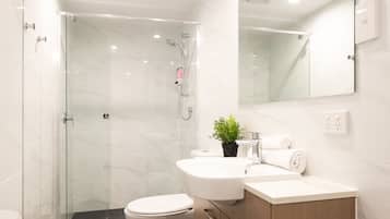 A modern bathroom with a glass shower enclosure, a white toilet, and a wooden vanity with a mirror.