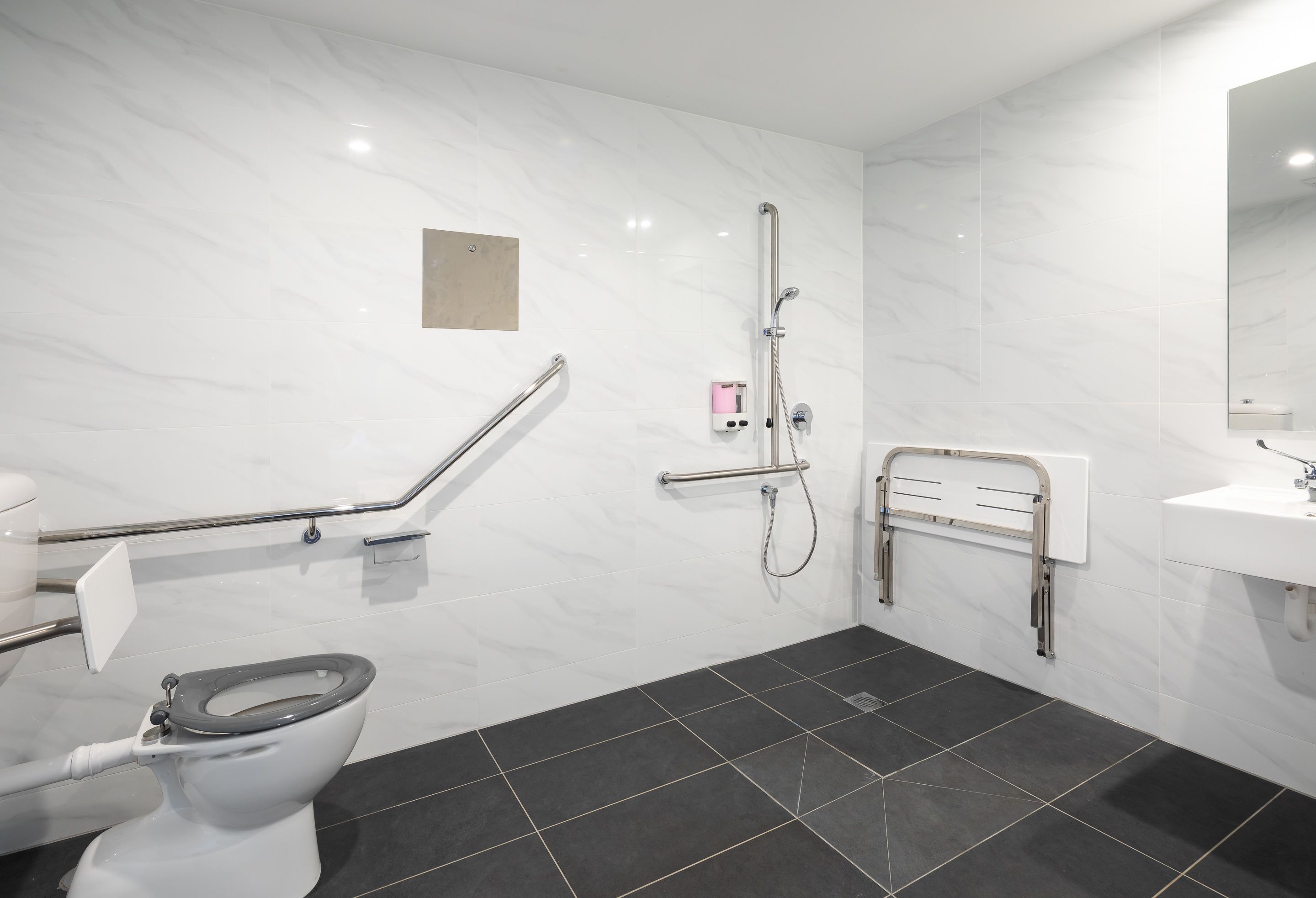 A modern bathroom with a toilet, grab bars, a shower, and a sink.