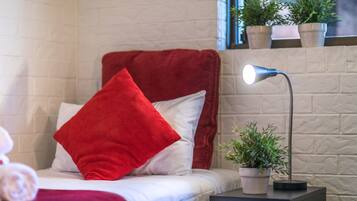 Een keurig opgemaakt bed met rode en witte kussens, een bedlampje en een kleine plant in een potje op een nachtkastje.