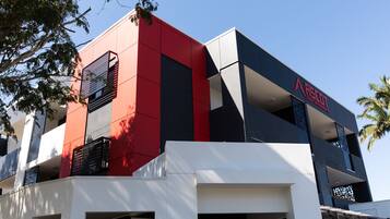 A multi-story building with a modern architectural design, featuring a prominent red and black facade and a visible logo on the upper right side.
