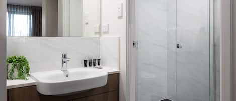 Un baño moderno con lavamanos blanco, tocador de madera y ducha con cerramiento de vidrio.