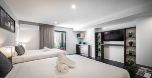 Ein modernes Hotelzimmer mit zwei Betten, einem Fernseher, einem Schreibtisch und einem Balkon mit Pflanzen.