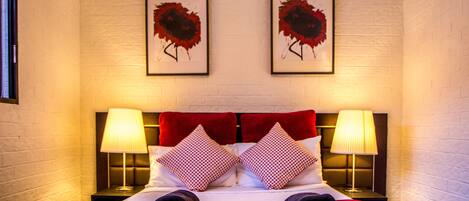 A hotel room with a bed, two wall-mounted lamps, and two framed artworks.