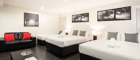 Habitación de hotel con dos camas, un sofá de cuero negro, una mesita de centro y dos lámparas fijadas a la pared.