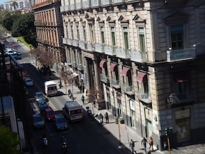 A street view with a row of buildings featuring classical architecture, a busy street with cars and a bus, and pedestrians. - Rooms 20 Settembre (Catania)