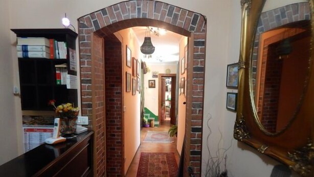 A hallway with a brick archway leading to a room with a green chair and a plant. - Rooms 20 Settembre (Catania)