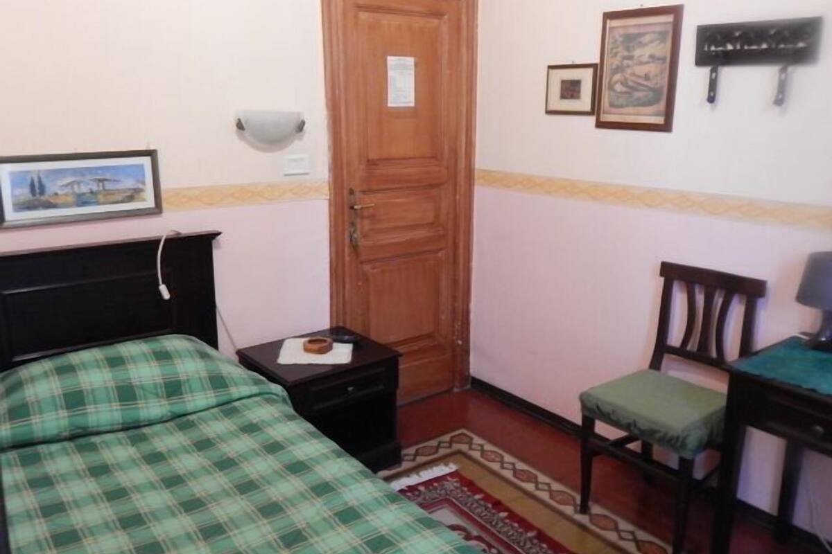 Un dormitorio con cama, mesita de noche, silla, escritorio y puerta.