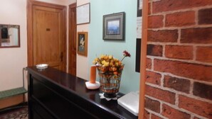 A reception area with a wooden desk, a vase of flowers, and a brick wall. - Rooms 20 Settembre (Catania)