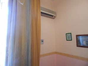 Una habitación con una pared color crema, un equipo de aire acondicionado blanco montado en la pared y un cuadro enmarcado colgado allí.