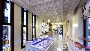 A corridor with a glass display case filled with various items, a white reception desk, and a patterned floor. - Casa Palacete 1822 (Granada)