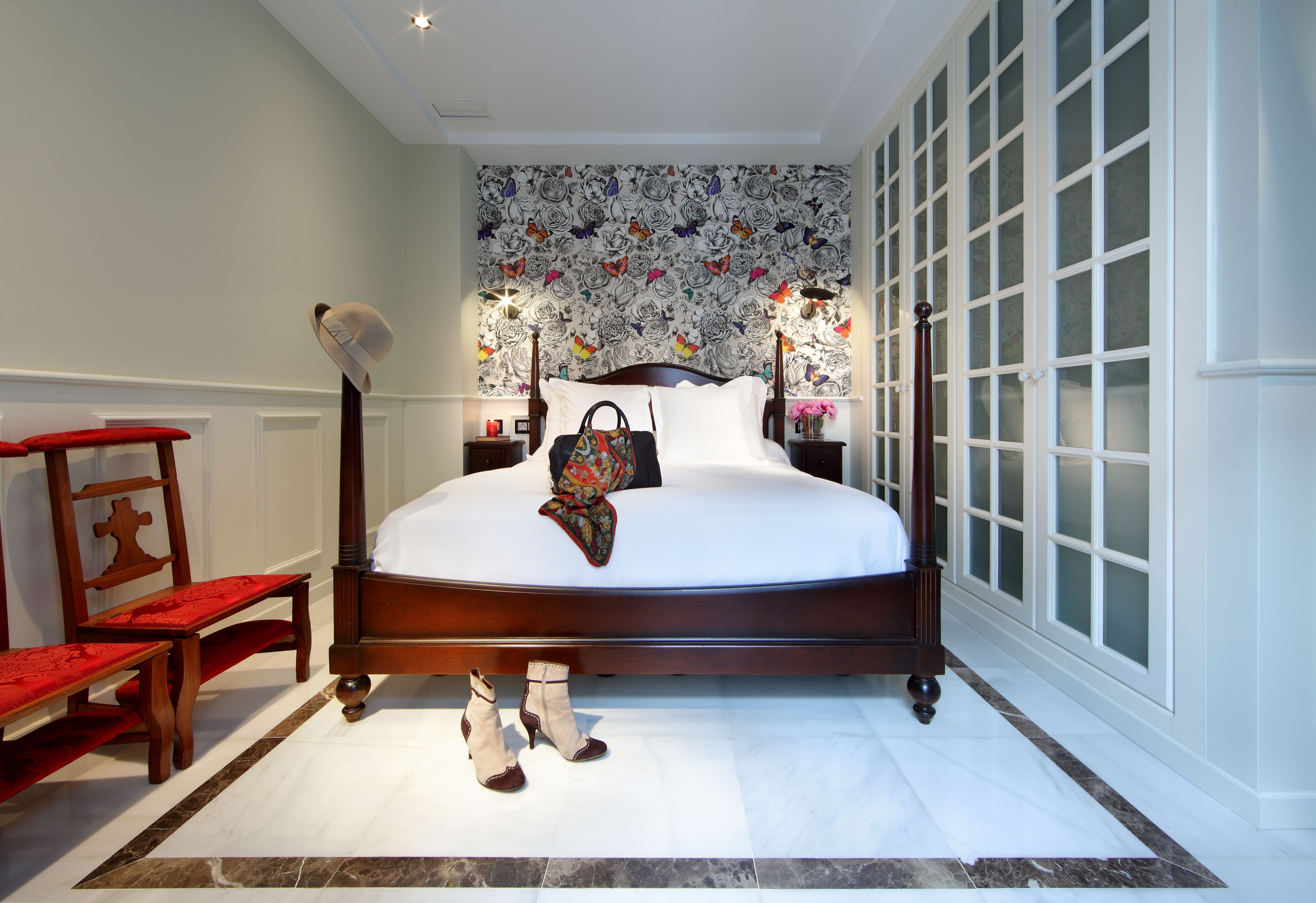 A neatly made bed with a floral-patterned headboard, a wooden nightstand with a lamp, and a red bench.