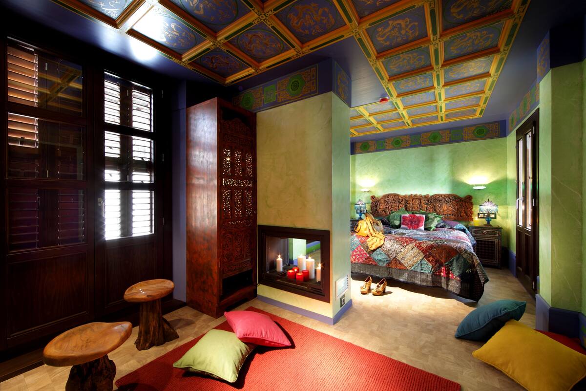A room with a large bed, a fireplace, a wooden door, and a window with blinds.