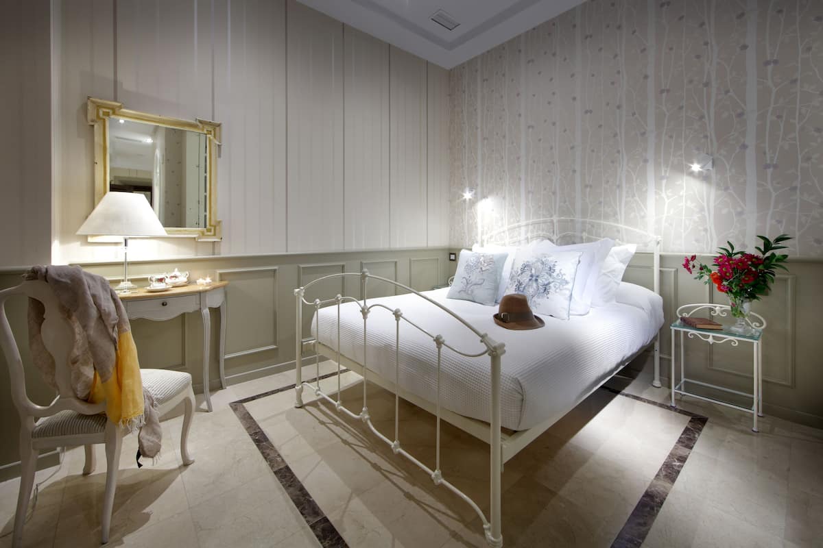 A neatly arranged bedroom with a bed, bedside table, lamp, chair, and a mirror.