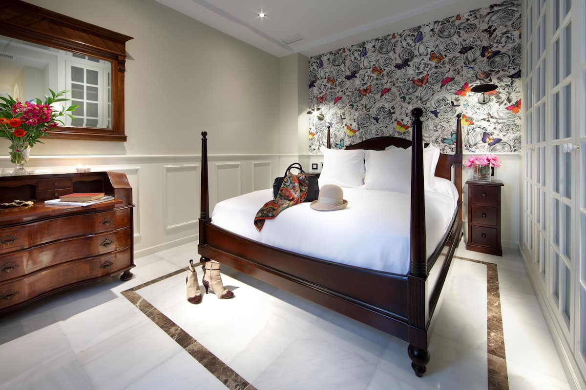 A bedroom with a four-poster bed, a dresser, a mirror, and a floral wallpaper.