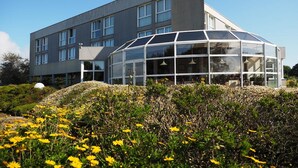 A modern building with a large glass conservatory, surrounded by a garden with yellow flowers. - Belvédère Hôtel (Brest)
