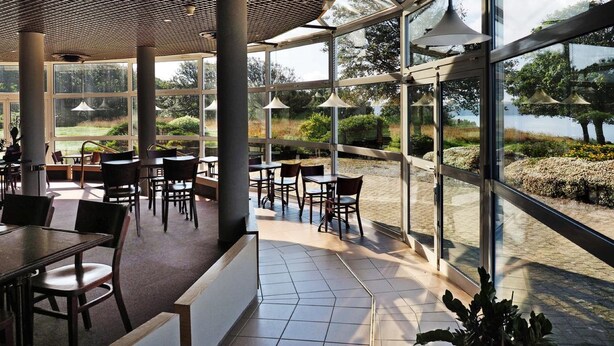 A spacious indoor area with large windows offering views of a landscaped garden and a body of water. - Belvédère Hôtel (Brest)