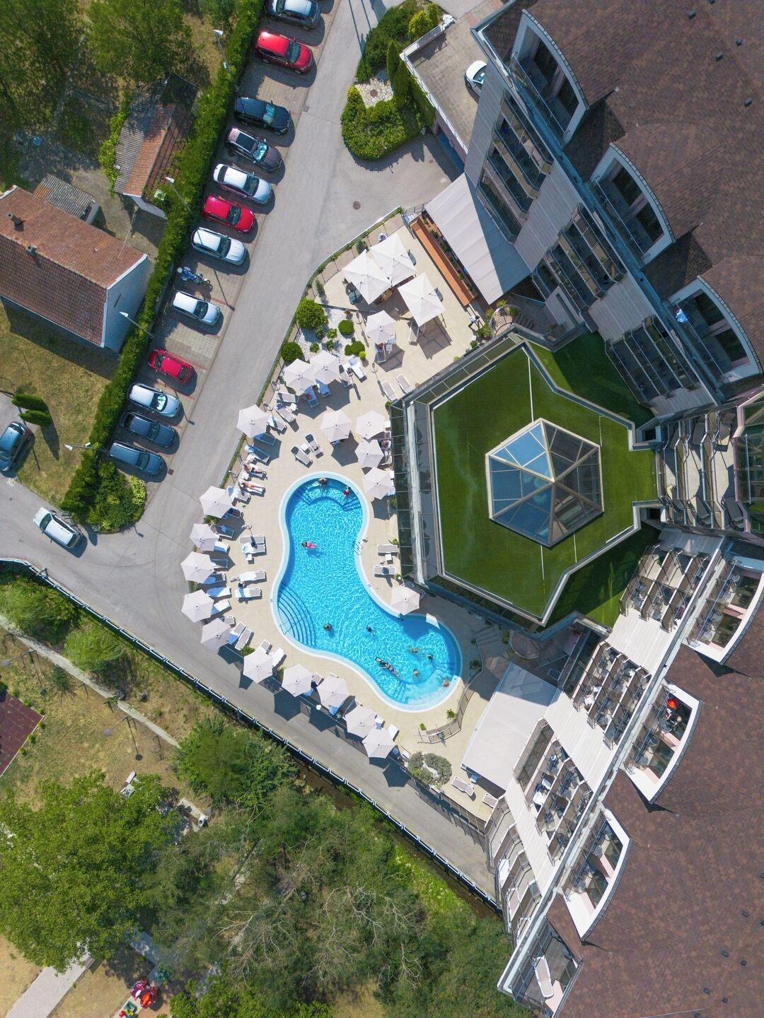 An aerial view of a hotel with a swimming pool, multiple parking spaces, and a modern building with a unique geometric design.