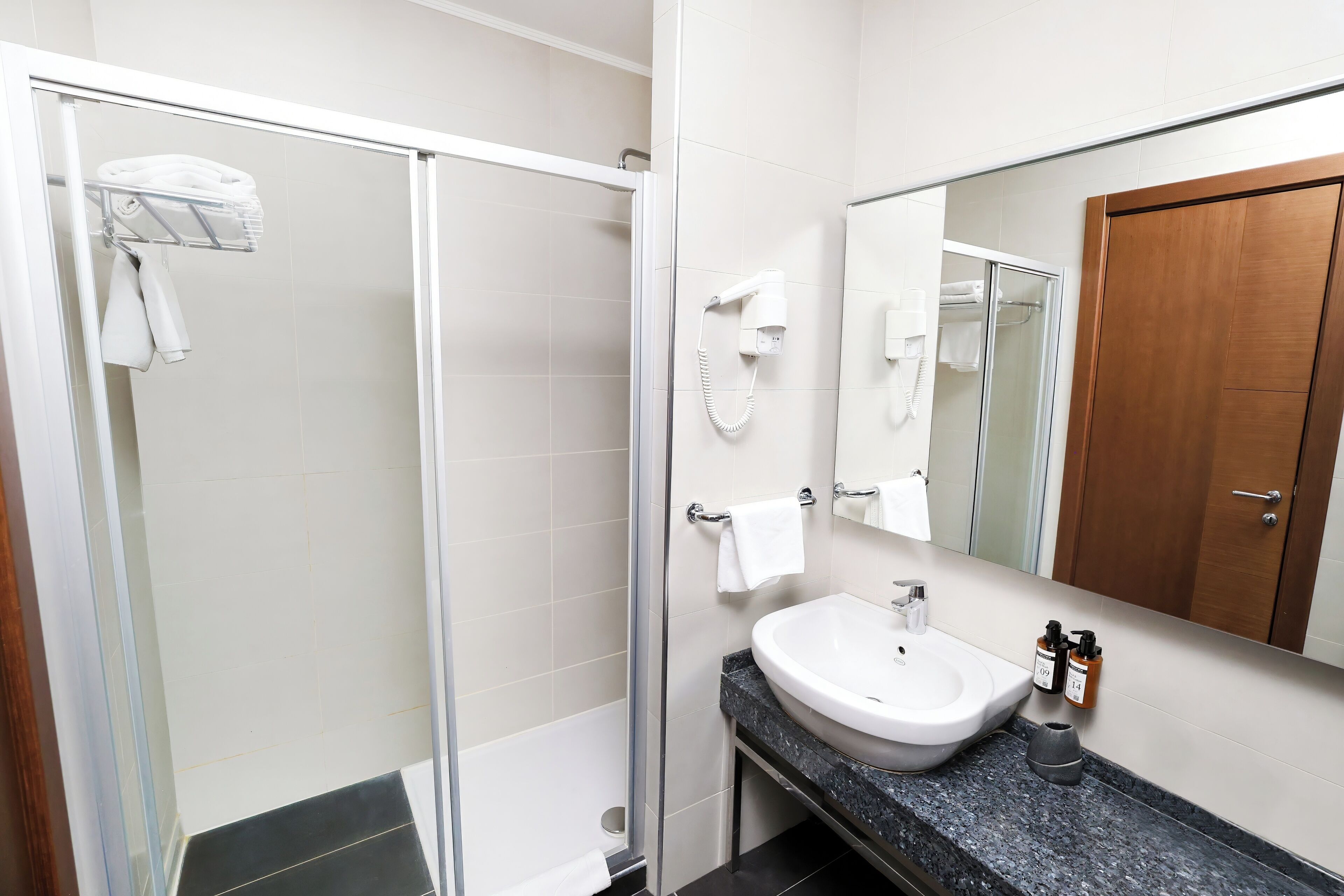 Un baño moderno con ducha envuelta en vidrio, un lavamanos blanco y un espejo grande.