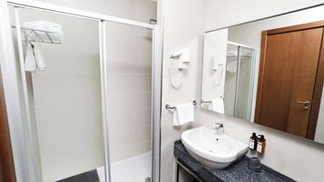 Un baño moderno con ducha envuelta en vidrio, un lavamanos blanco y un espejo grande.