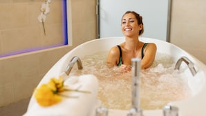 Una mujer en una bañera llena de burbujas, con una toalla y una flor en el borde.
