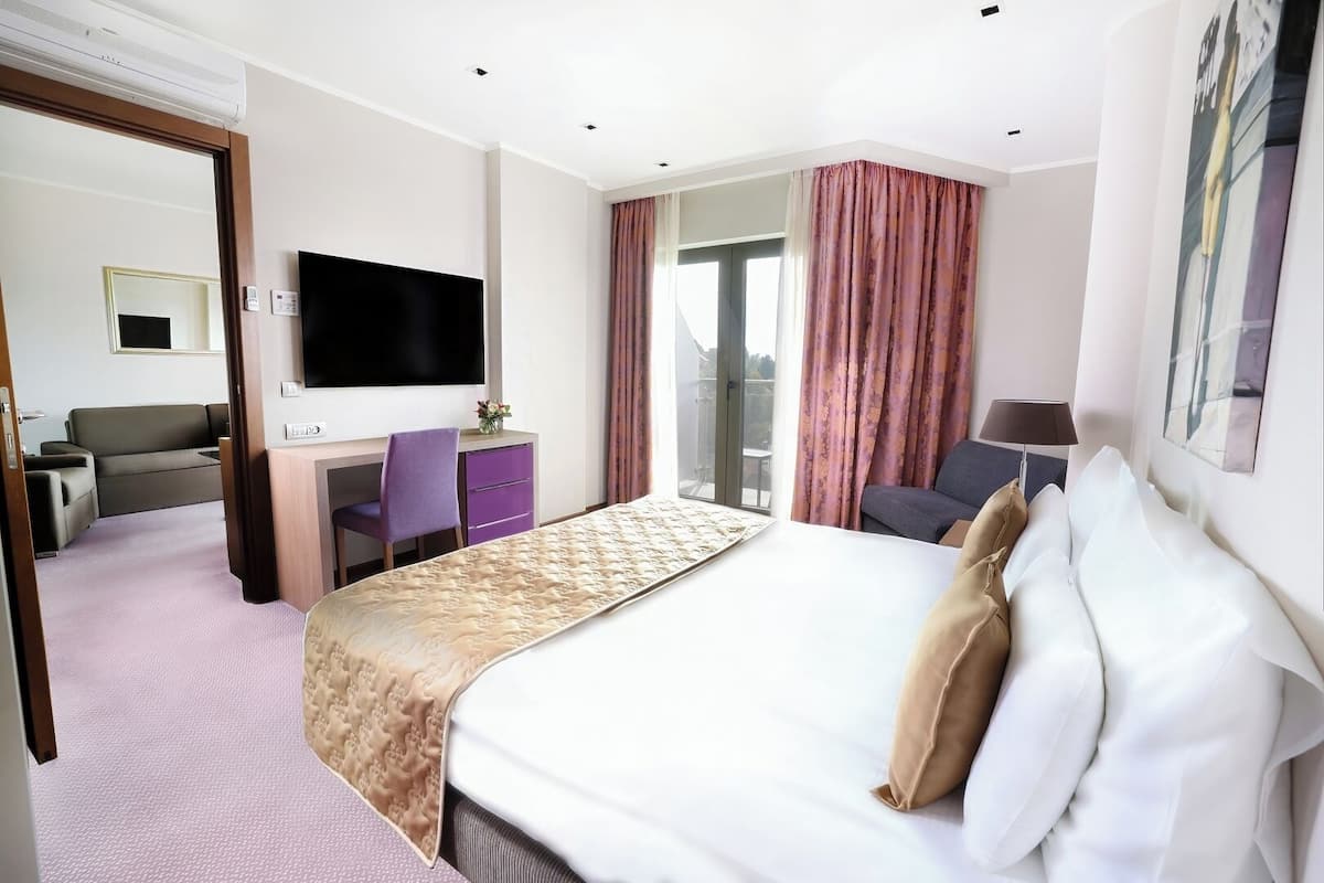 Ein Hotelzimmer mit Bett, Schreibtisch mit Stuhl, Fernseher und einem Balkon mit Vorhängen.