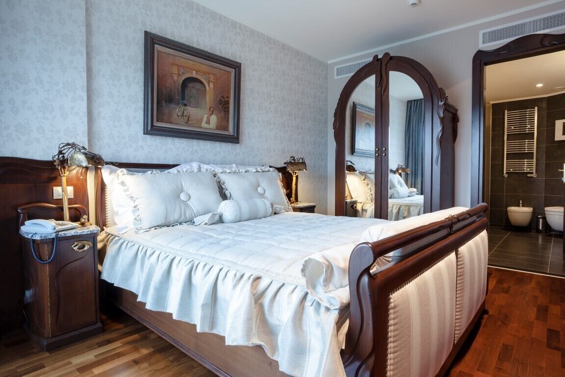 A bedroom with a large bed, a nightstand, a mirror, and a painting on the wall.