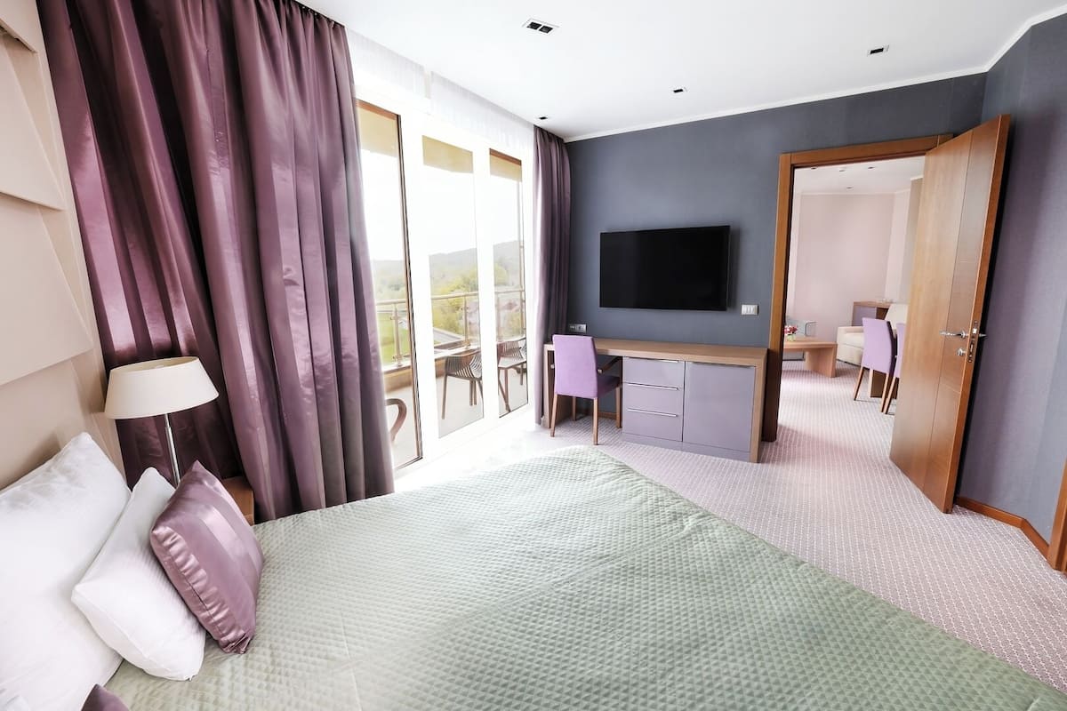 Ein Hotelzimmer mit Bett, Schreibtisch, Fernseher und einem Balkon mit Vorhängen.