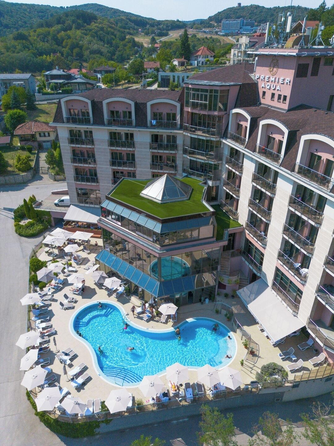 A hotel with a rooftop pool, multiple balconies, and a view of surrounding hills.
