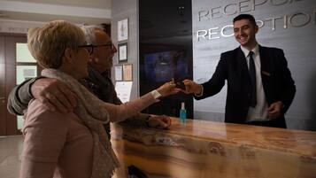 A reception desk with a man in a suit handing over a card to two people.