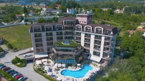 Un hotel de varios pisos con un área de piscina central, rodeado de exuberante vegetación y un paisaje montañoso.