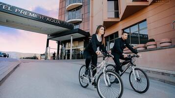 Two people riding bicycles in front of a hotel named "EL PREMIER AQUA".