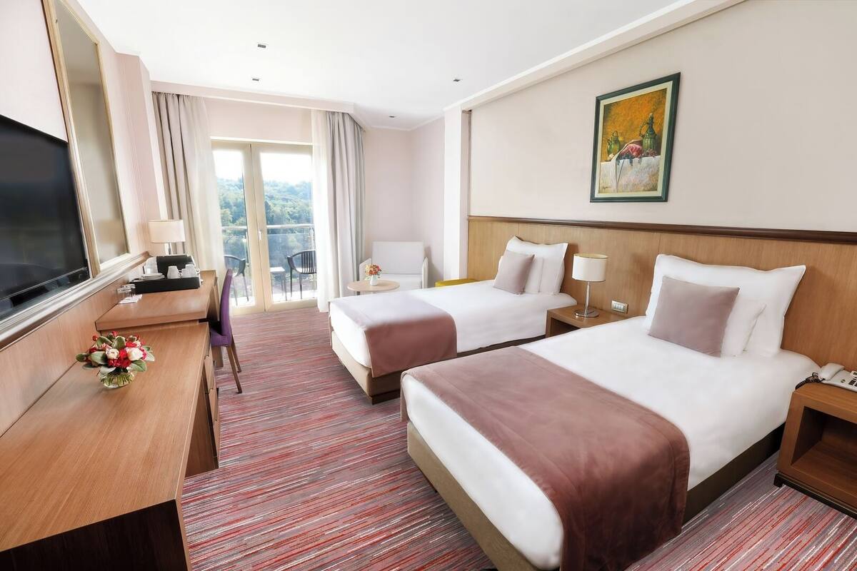 Ein Hotelzimmer mit zwei Betten, einem Schreibtisch, einem Fernseher und einem Balkon mit Blick.