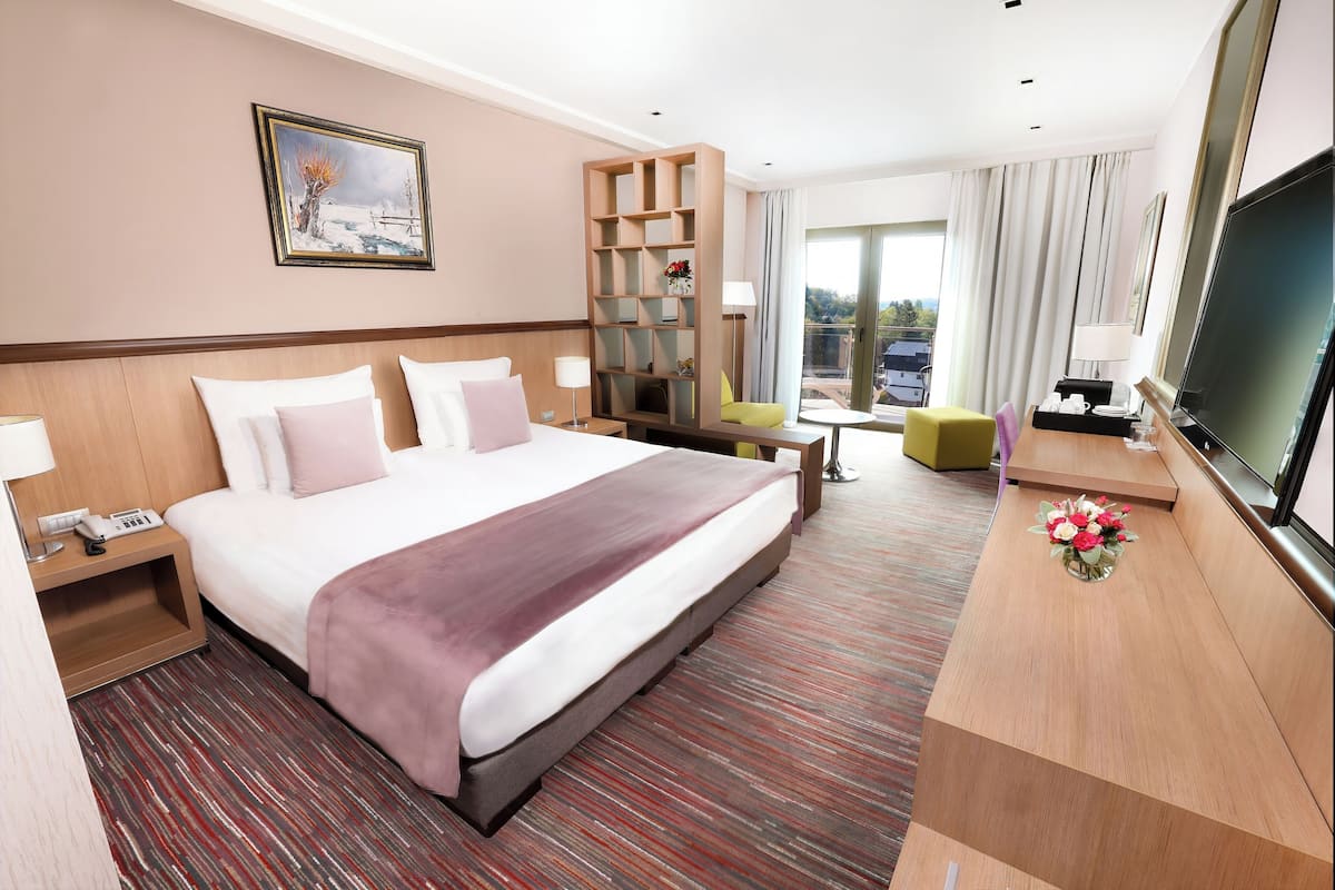 Ein Hotelzimmer mit einem großen Bett, einem Schreibtisch, einem Fernseher, einem Bücherregal und einem Fenster mit Aussicht.