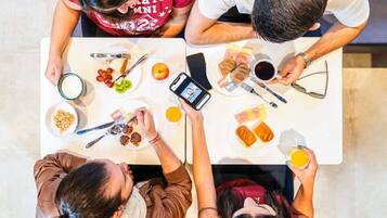Un groupe de personnes est assis autour d’une table, devant de la nourriture et des boissons, un téléphone intelligent et un ordinateur portable.