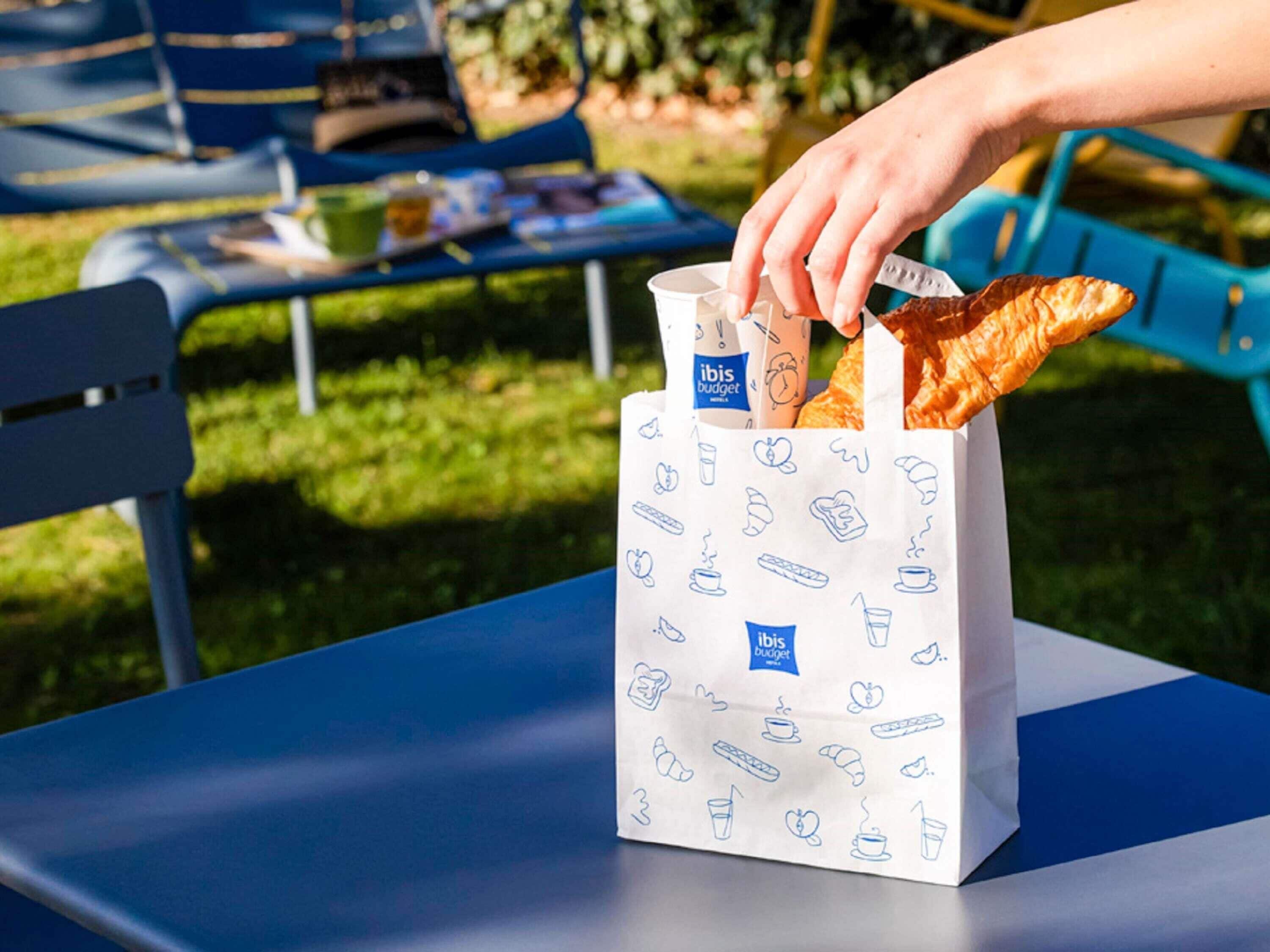 A white paper bag with blue text and food illustrations, placed on a blue table.