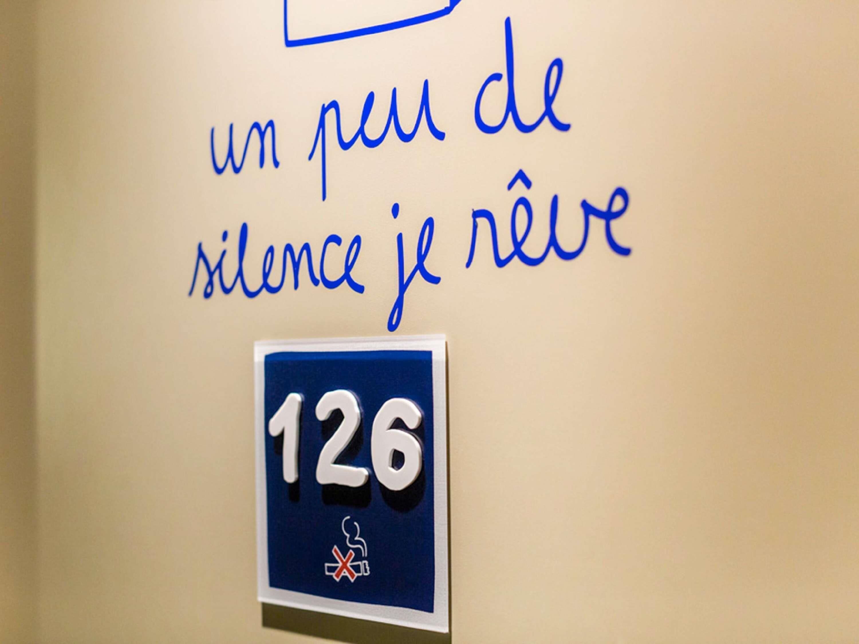 Un mur avec une pancarte sur laquelle on peut lire « un peu de silence, je rêve » et un numéro de chambre, le « 126 », accompagné d’un symbole interdisant de fumer.