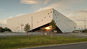 Un edificio moderno de diseño geométrico y original, con una entrada amplia y un espacio abierto circundante con árboles.