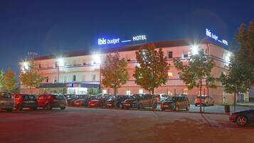 A hotel with a sign reading "ibis budget HOTEL" and multiple parked cars in the foreground.