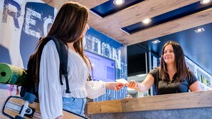 Una persona sostiene un monopatín en un mostrador con techo de madera y pared azul con texto.