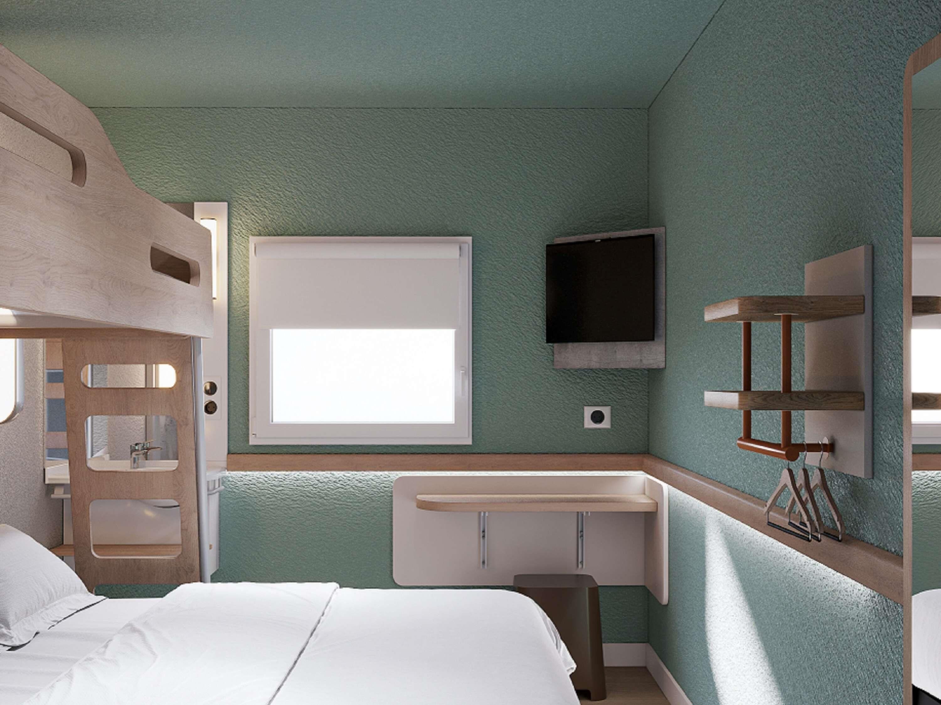 Une chambre d’hôtel de taille réduite, comprenant un lit, un petit bureau, un miroir, une télévision et une fenêtre.
