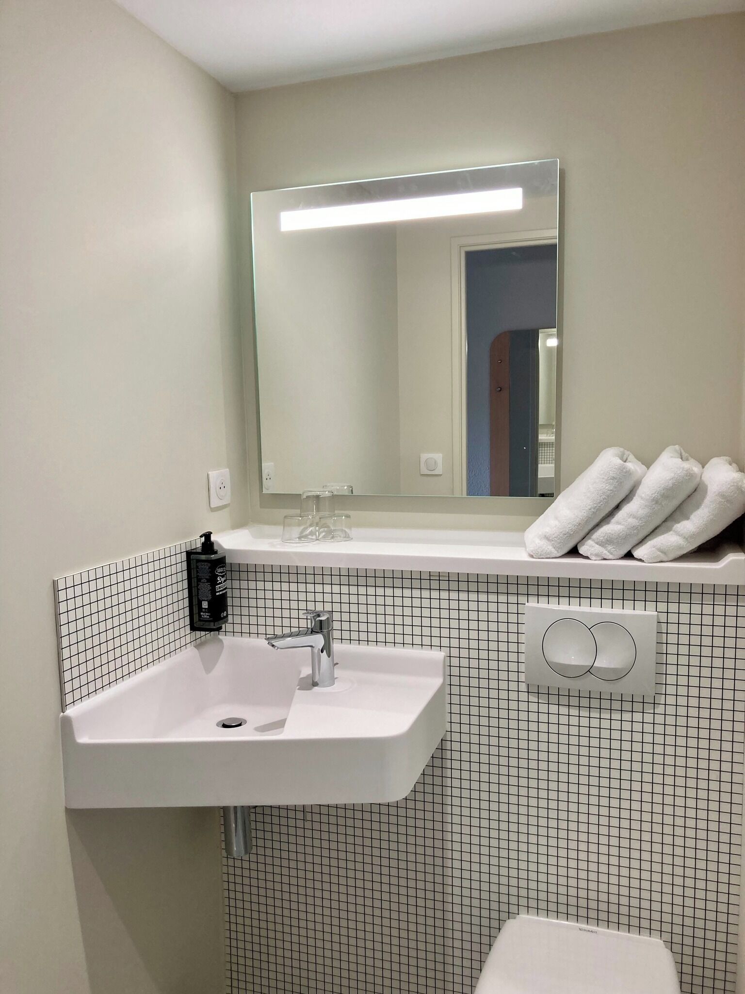 Une salle de bain avec un lavabo blanc, un miroir et un porte-serviettes avec des serviettes.