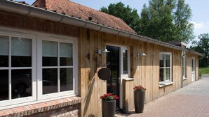 A wooden building with large windows, a brick base, and two large flower pots on the ground. - B&B Erve Fakkert (Rossum)